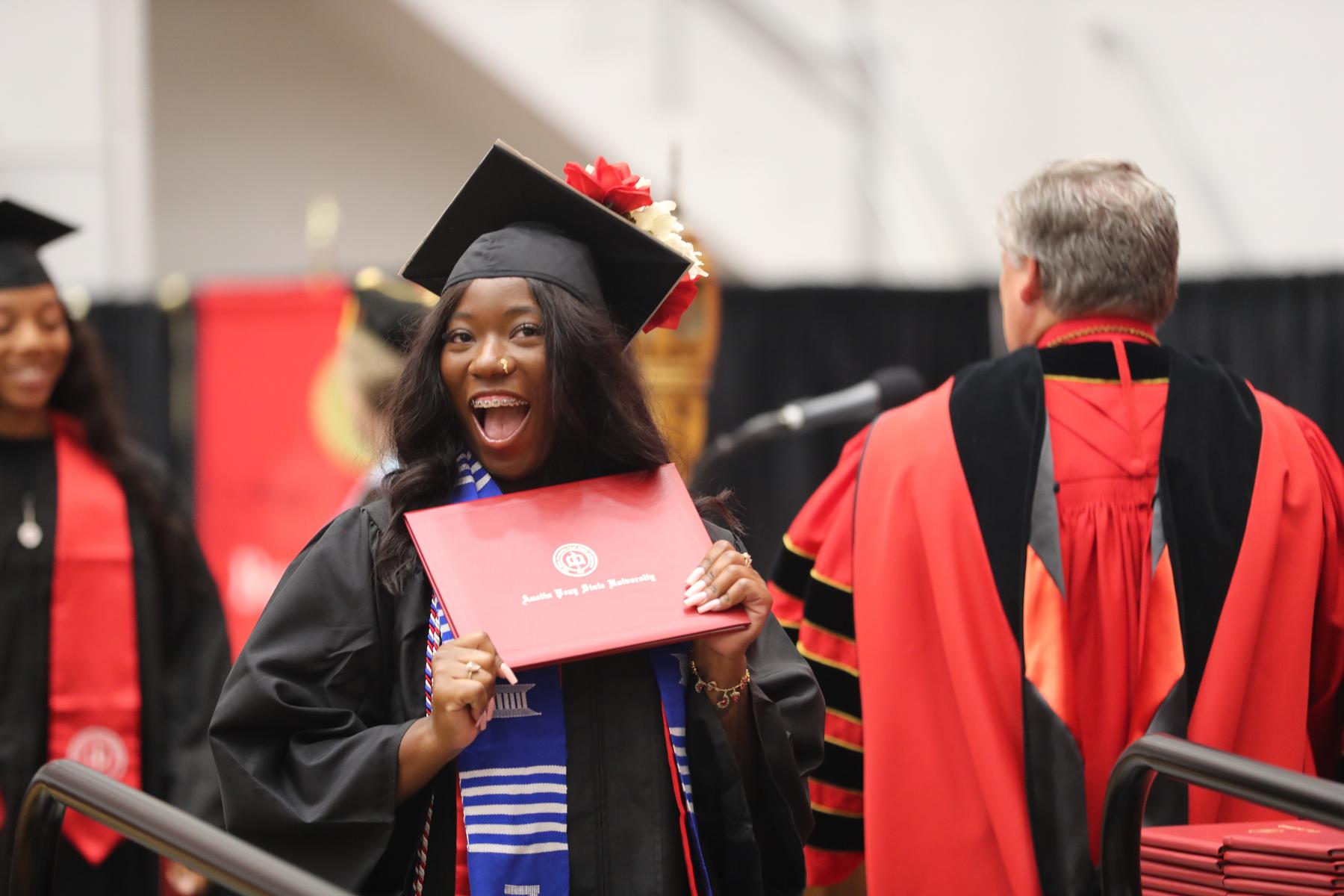 Student smiling while holding their diploma at graduation