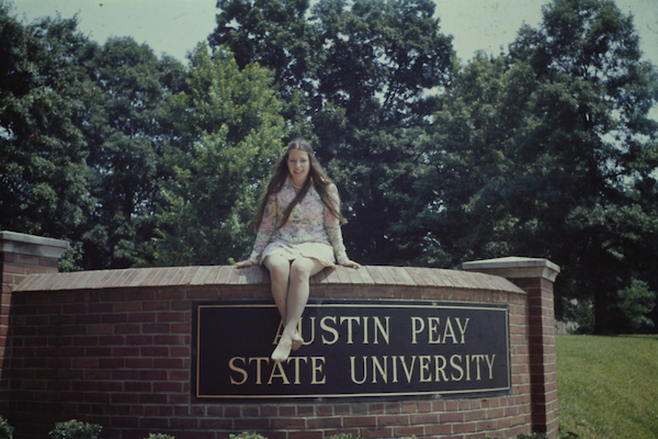 A student in the early 1970s sits on the APSU gateway sign.