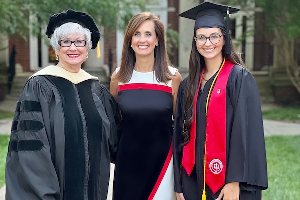 The three members of the Holleman-Reagan family stand on campus in commencement regalia.