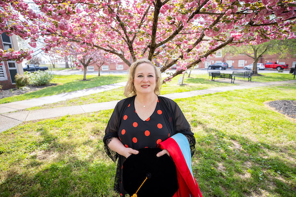 Sarah Dugger stands on campus, holding her graduation gown.