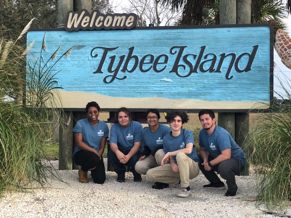 APSU students kneeling in front of a Tybee Island sign