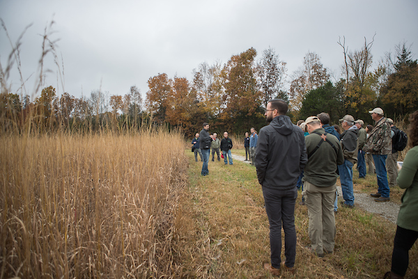Dr. Dwayne Estes, dressed in a coat, leads a tour through brown grasslands in the fall.