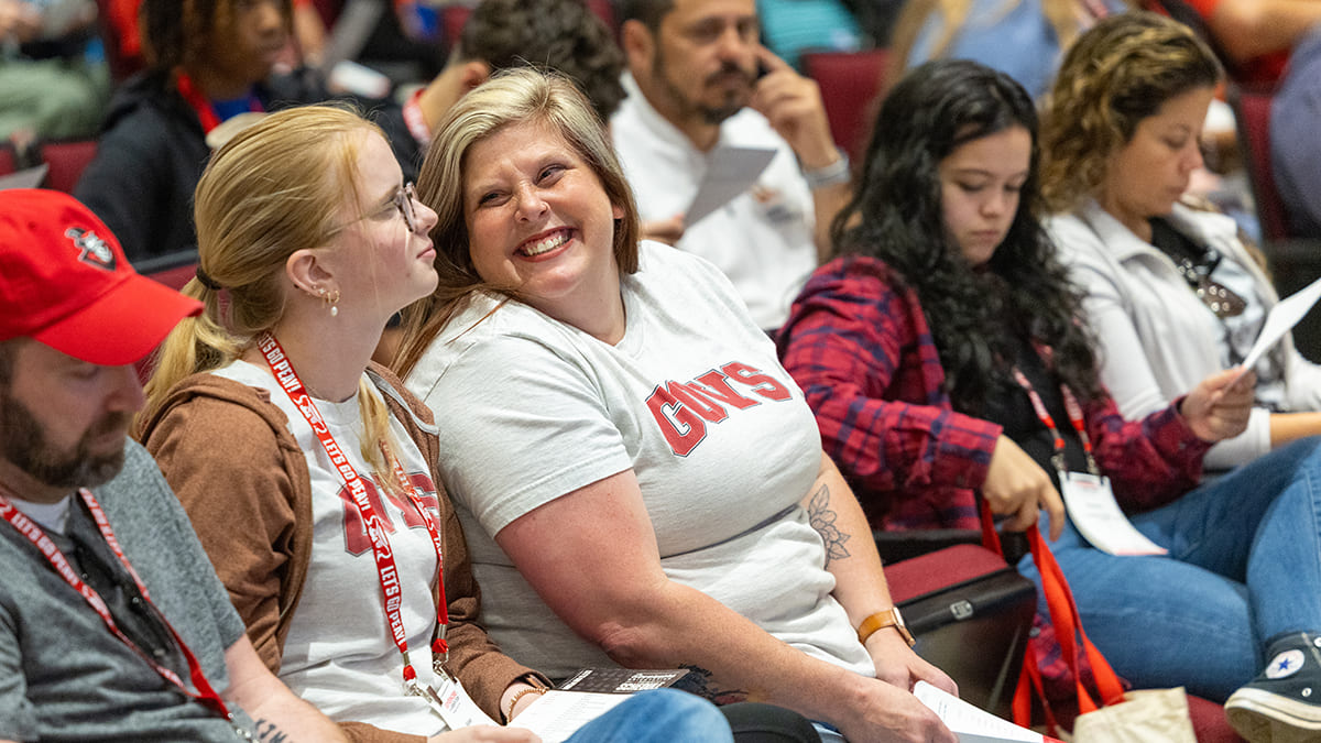 A mother smiling at her daughter while sitting in the crowd at orientation.