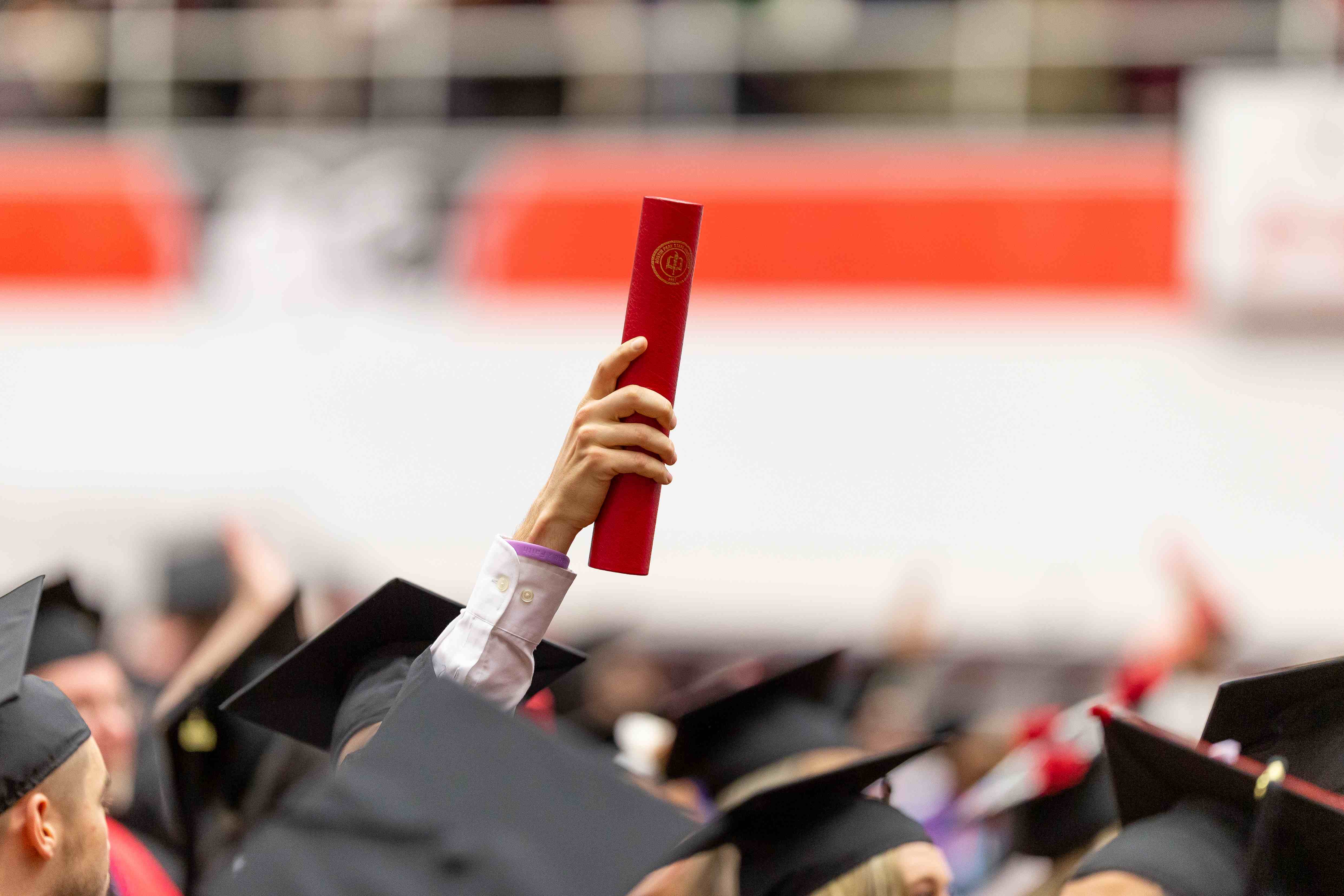 graduate holds up diploma over a sea of graduates