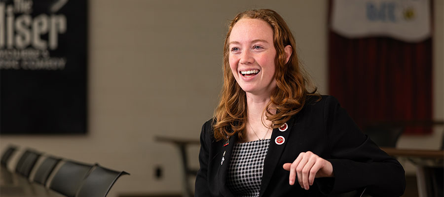 Female student in business attired sitting at a table and engaging in an interview with someone behind the camera.