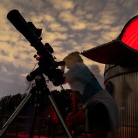 A long-exposure, nighttime photo of ghostly figures of people looking through and moving around a telescope beside the APSU Observatory.