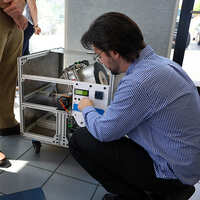 An engineering student kneels beside a machine he's built.