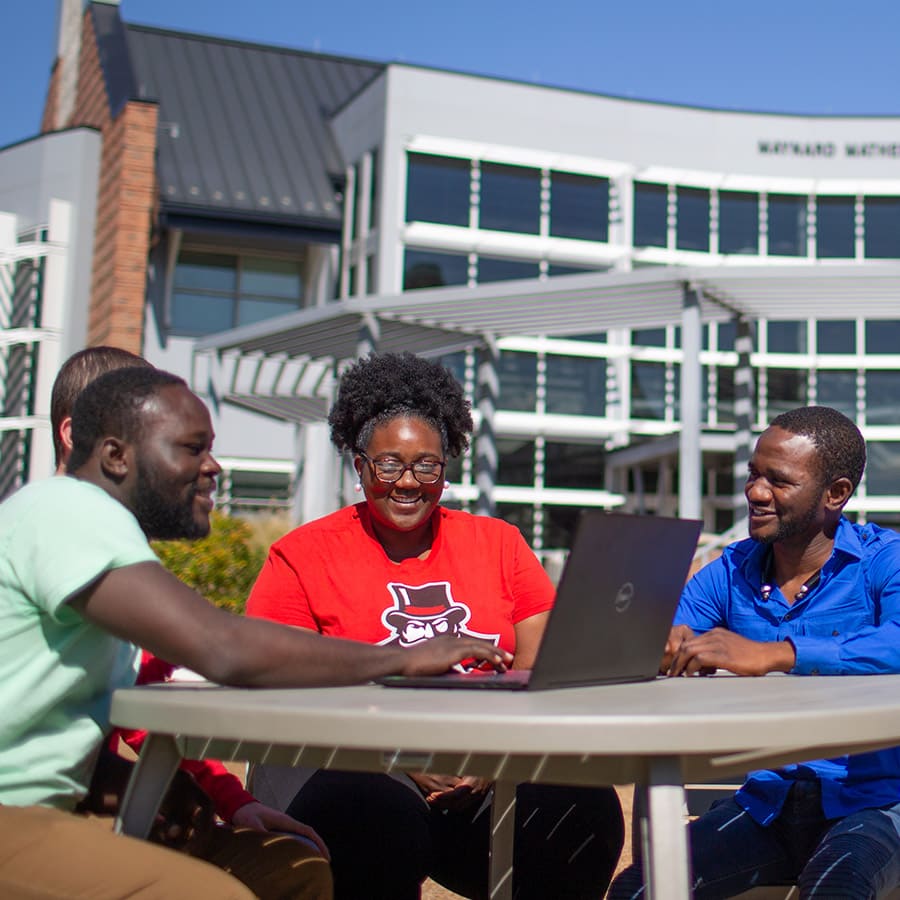 A group of students sitting at an outdoor table with a laptop in front of the Math and Computer Science building.