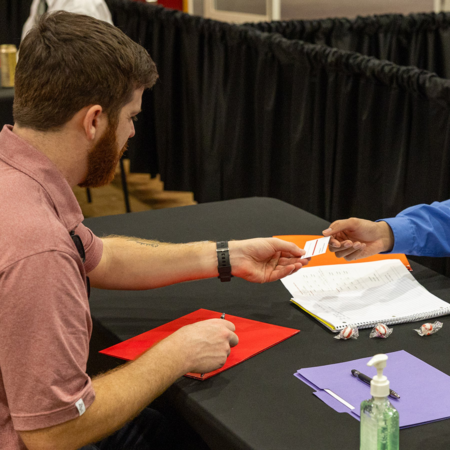 Two business people exchange a business card at a table during a career fair.