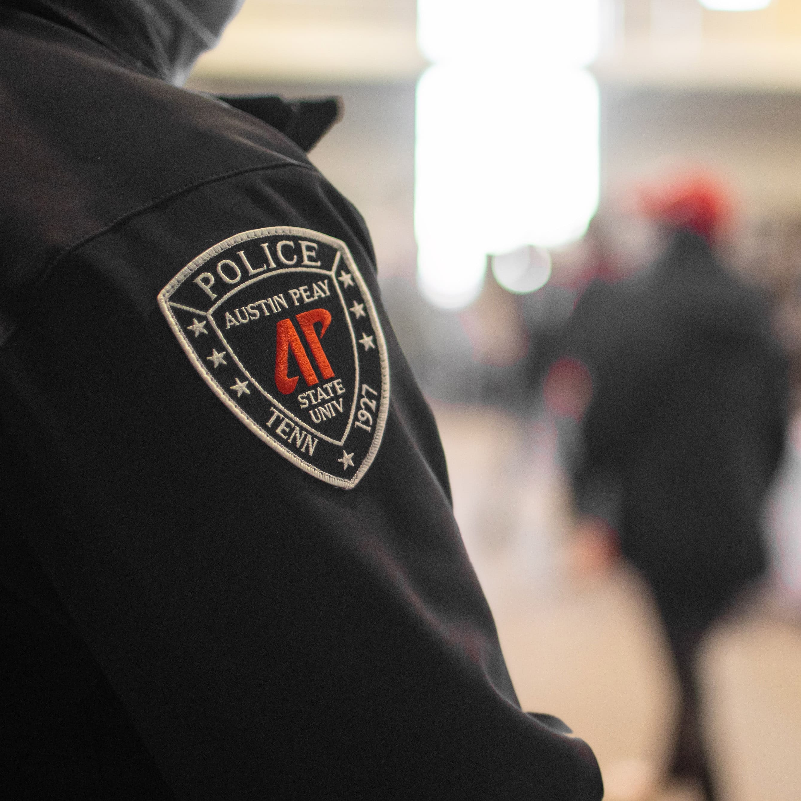 A police officer's shoulder patch in focus, in a busy indoor setting.