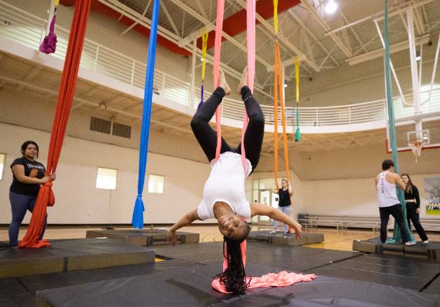 student doing aerial silks pose, hanging upside down