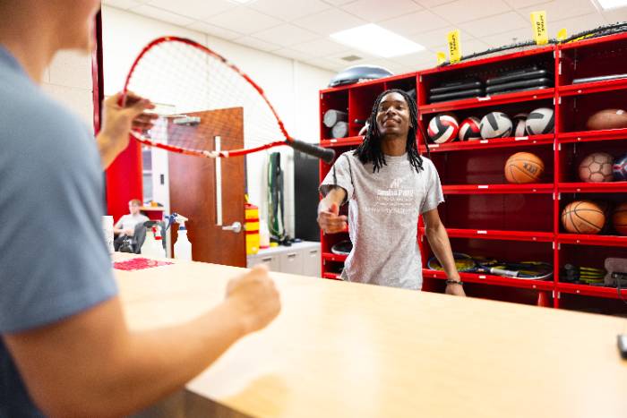 Foy Center student employee handing a student a raquet at equipment checkout desk