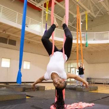 student doing aerial silks pose, hanging upside down