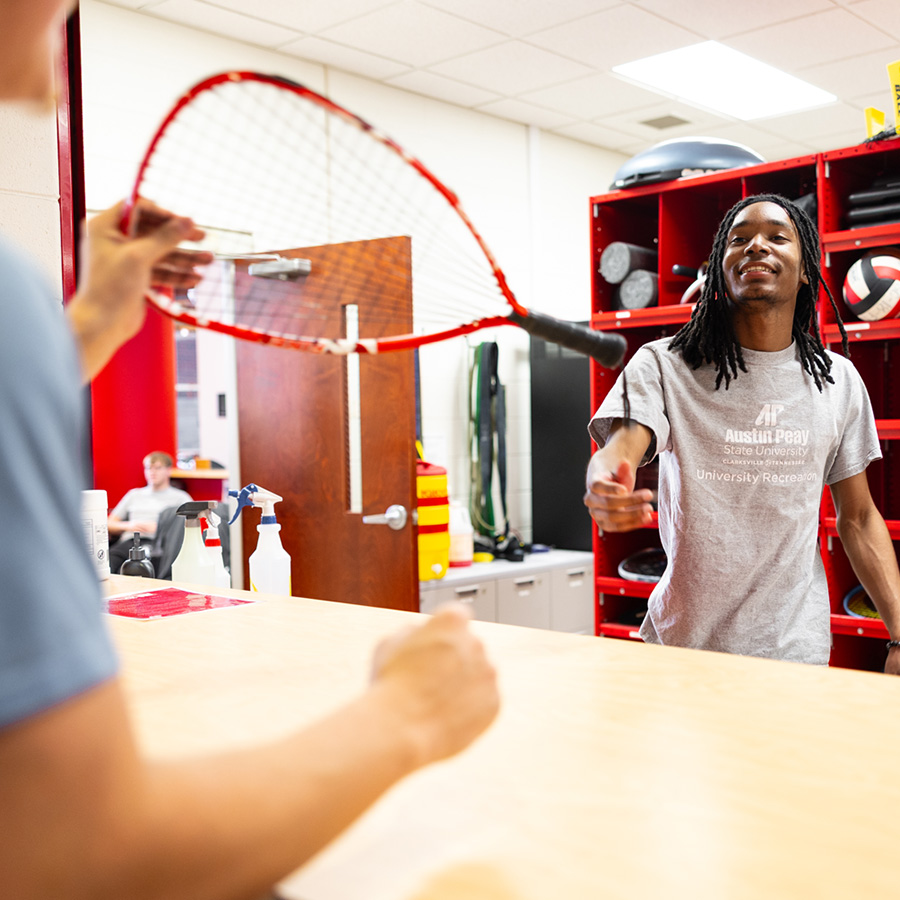 A University Recreation employee handing a student a racket to checkout.