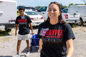A student and staff member smile while pulling carts behind them outdoors.