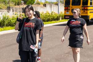 A group of students and staff walking away from a school bus in the sunshine.
